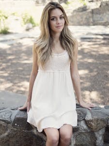 Portrait of a young woman in a white dress sitting outdoors on a sunny day.